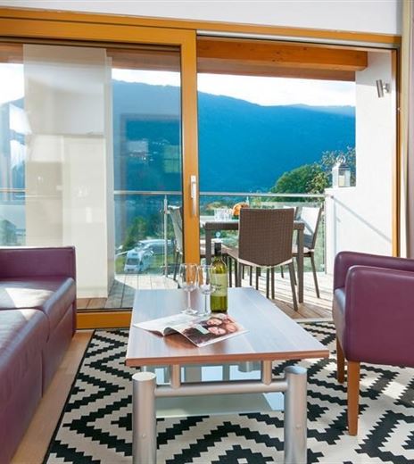 Ein stilvolles Wohnzimmer mit einem lila Sofa und einem Sesseln. Große Fenster bieten einen schönen Blick auf die Landschaft.